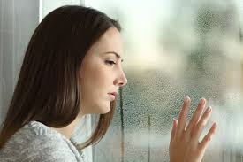 wistful woman looking out wet window